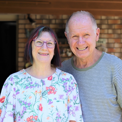 A photo of Robert and Cheryl smiling together out in their sunny front yard, at home A photo of Robert and Cheryl smiling together out in their sunny front yard, at home