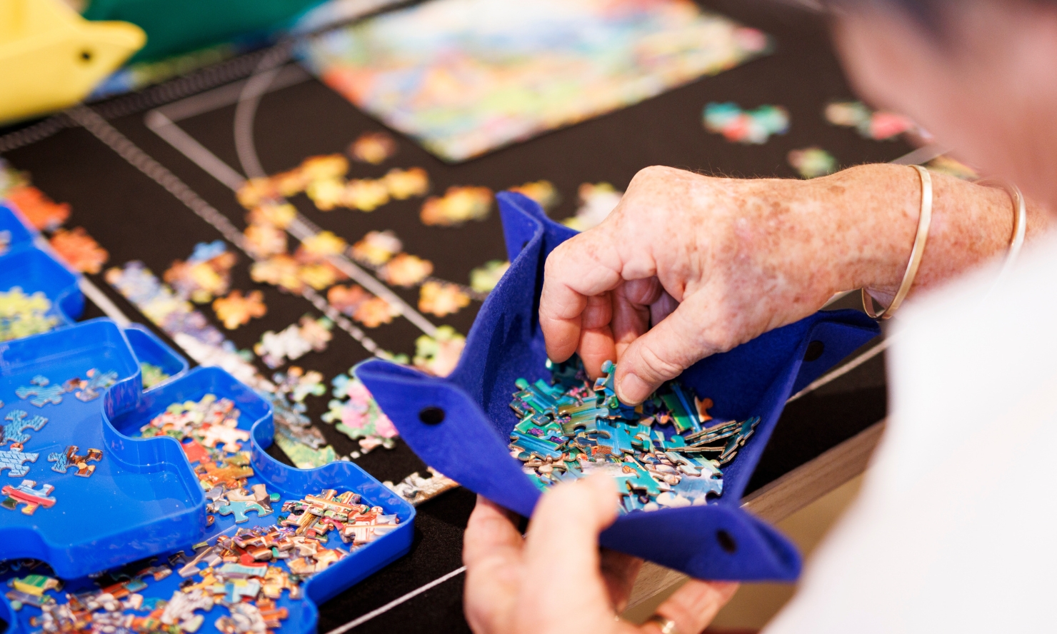 A person sorts through blue puzzle pieces in a blue tray while assembling a jigsaw puzzle.