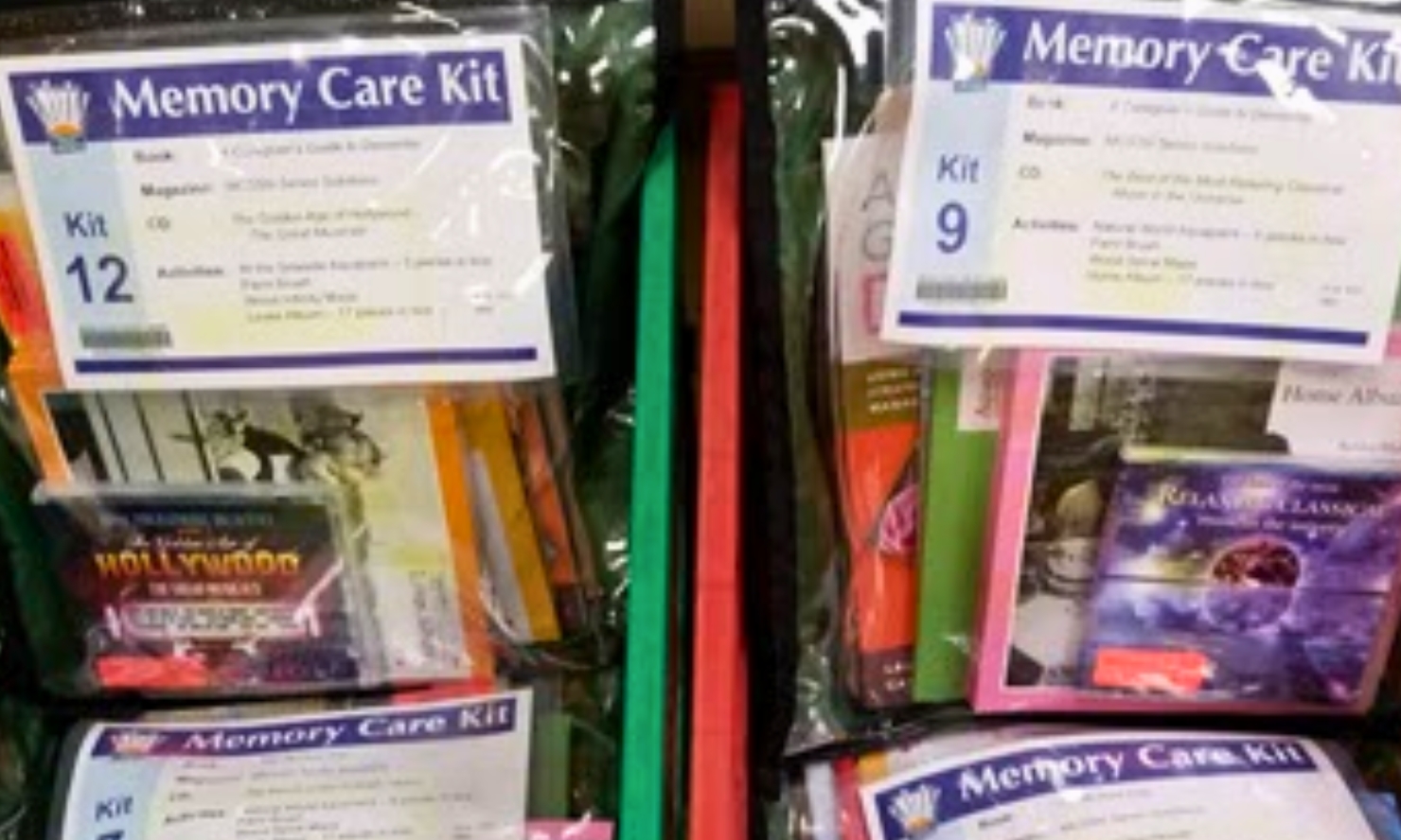 Several 'Memory Care Kits' are displayed in clear plastic bags, with labels indicating kit numbers and contents like books, magazines, CDs, and activities. Some kits contain items related to Hollywood and classical music.