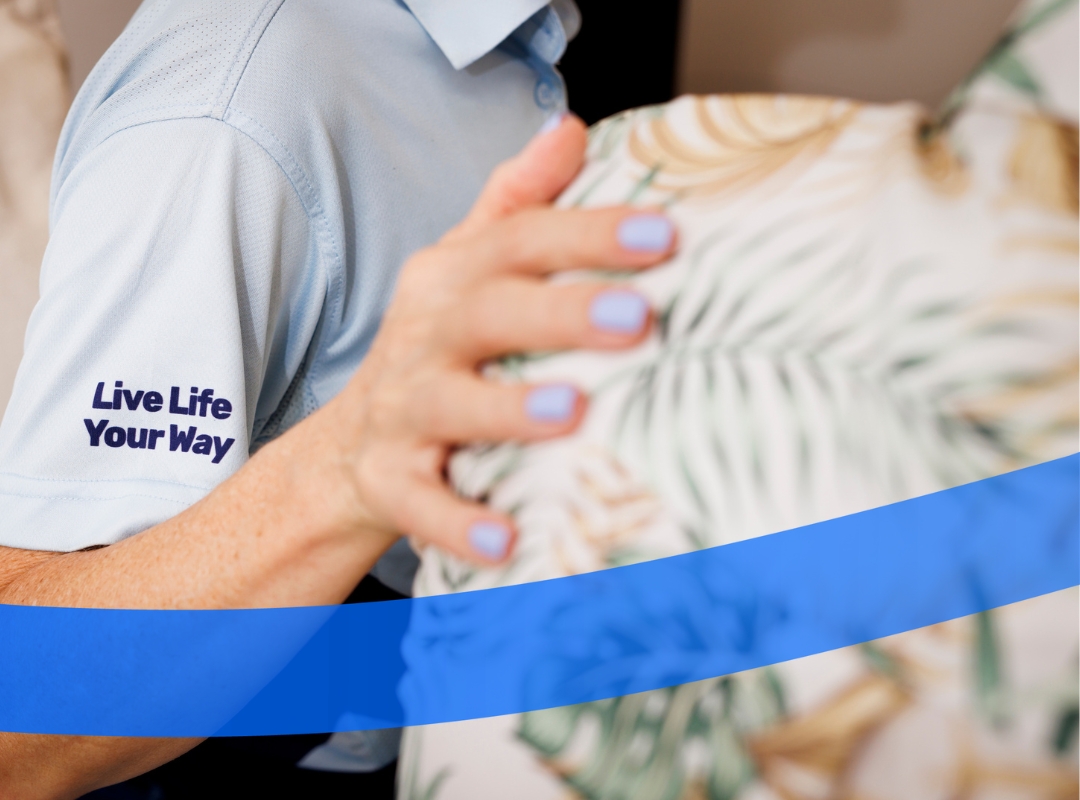 A close-up of a hand of a BlueCare team member on the shoulder of an older Queenslanders.